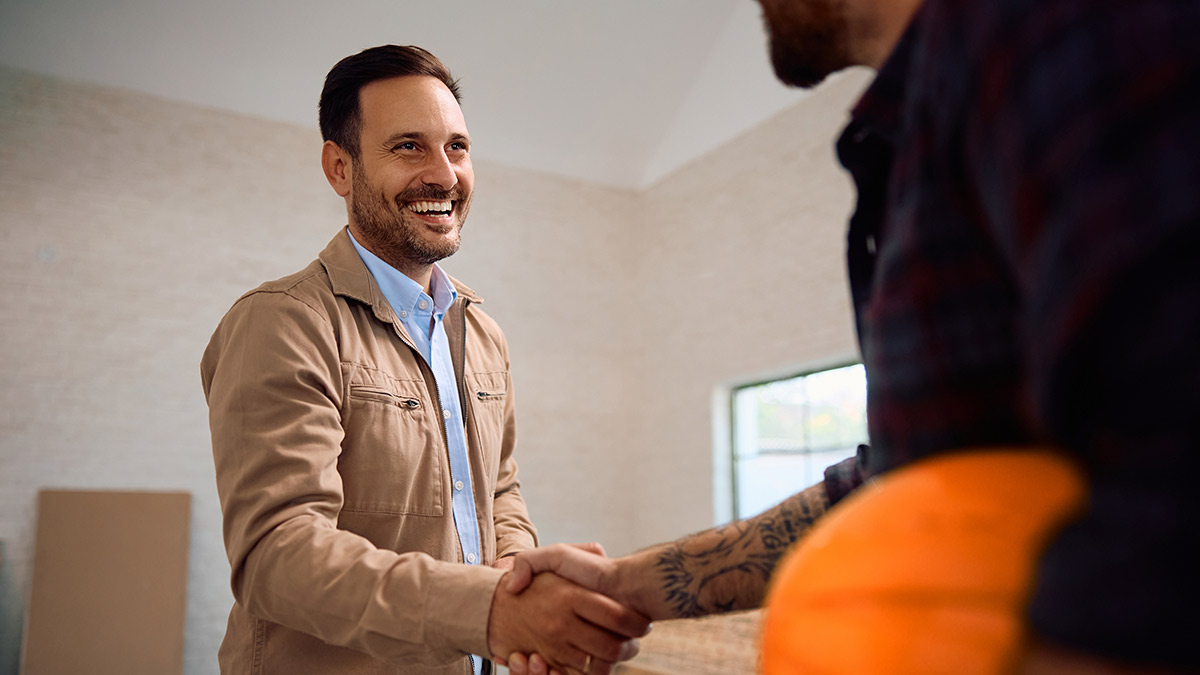 Two men shake hands in a home setting, representing collaboration or a business relationship.