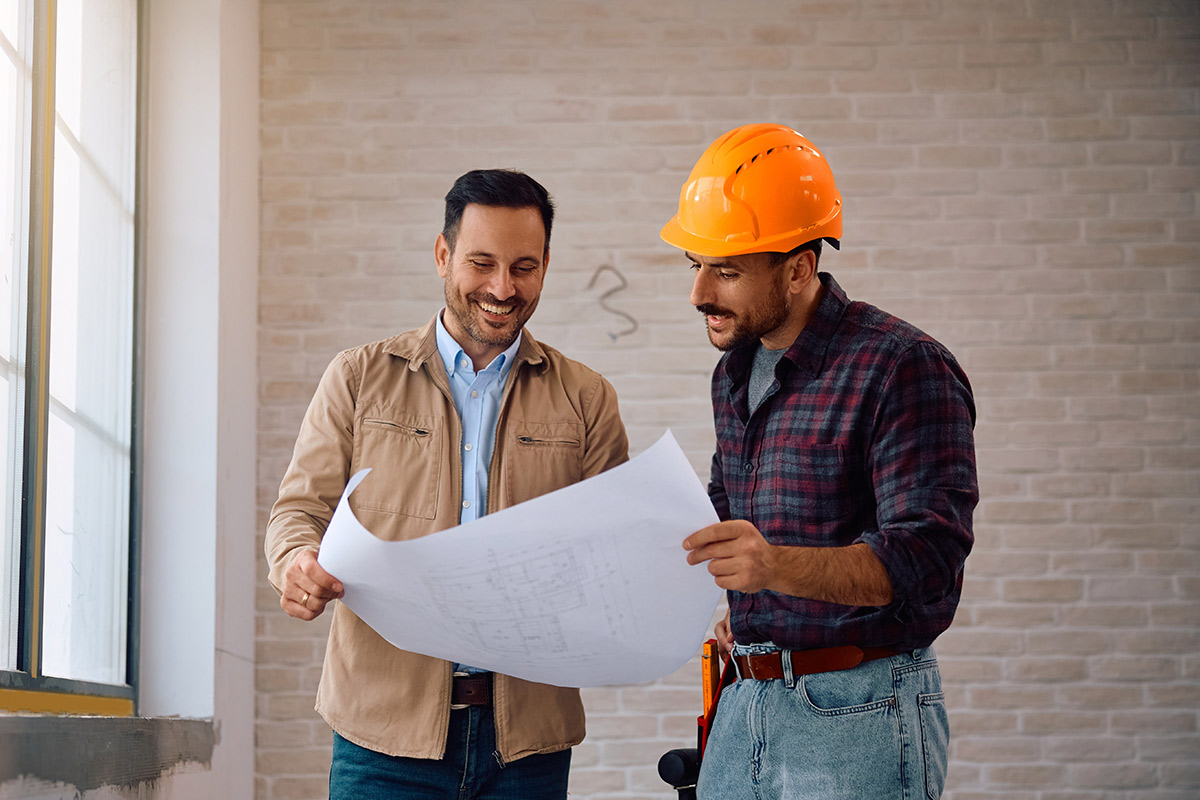 two men wearing hard hats review blueprints together, collaborating on construction plans and project execution.