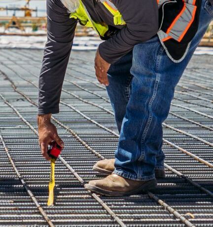 A construction worker uses a caliper to measure the thickness of a steel beam on a construction site.