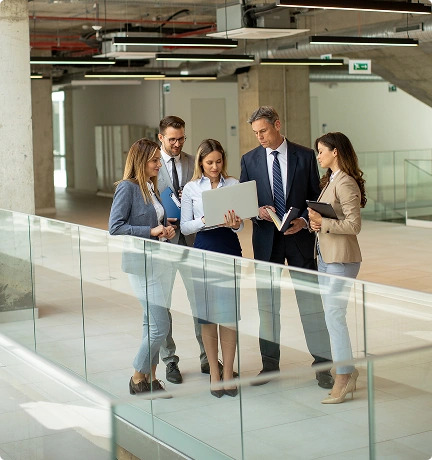 A group of business people in formal attire standing in an office building, discussing a program management