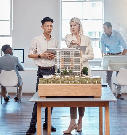 Two people stand in front of a detailed model of a building, discussing its design and features