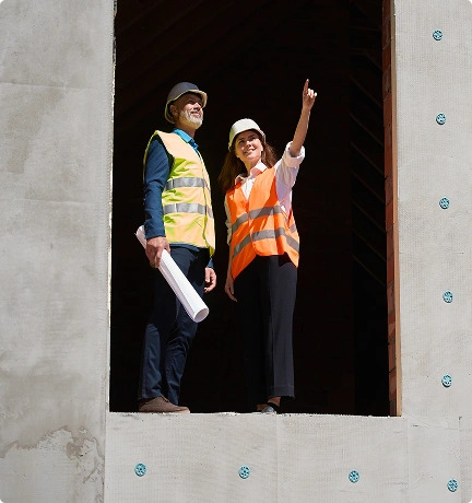Two individuals in construction vests standing together in a window, overlooking the surrounding area
