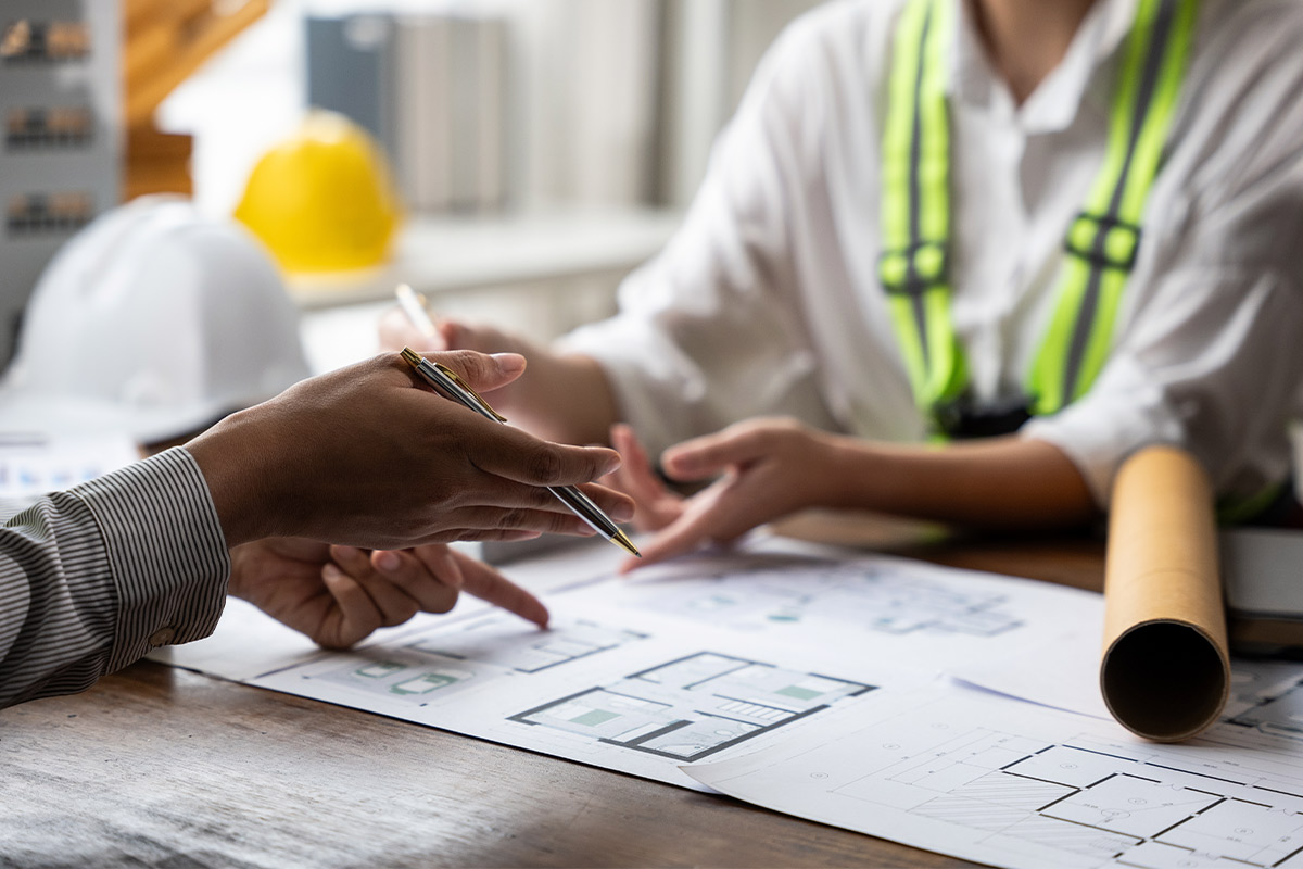 A man and woman engaged in a construction project, analyzing plans and addressing potential scheduling issues.
