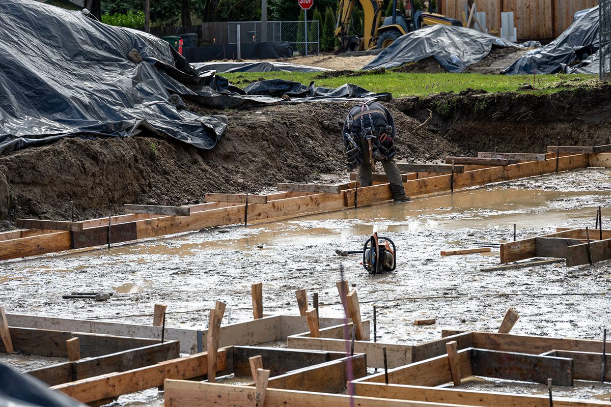 A man is constructing a concrete foundation in muddy conditions, illustrating potential construction schedule issues.