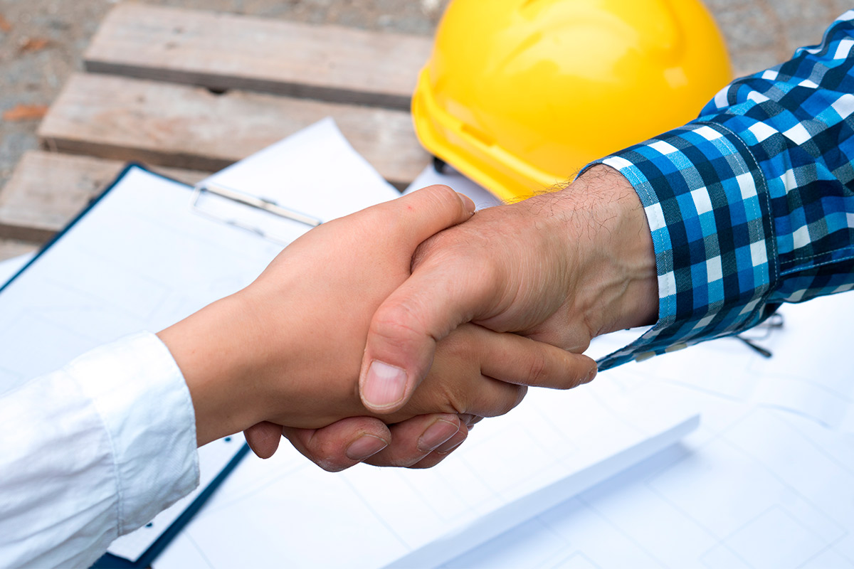 A man and woman shaking hands on a construction site, representing teamwork in addressing schedule challenges.