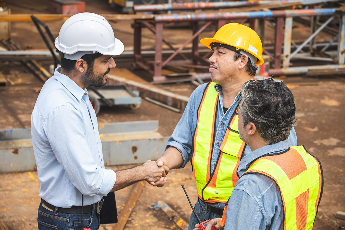Three men in hard hats shake hands, highlighting partnership in tackling essential construction project risks.