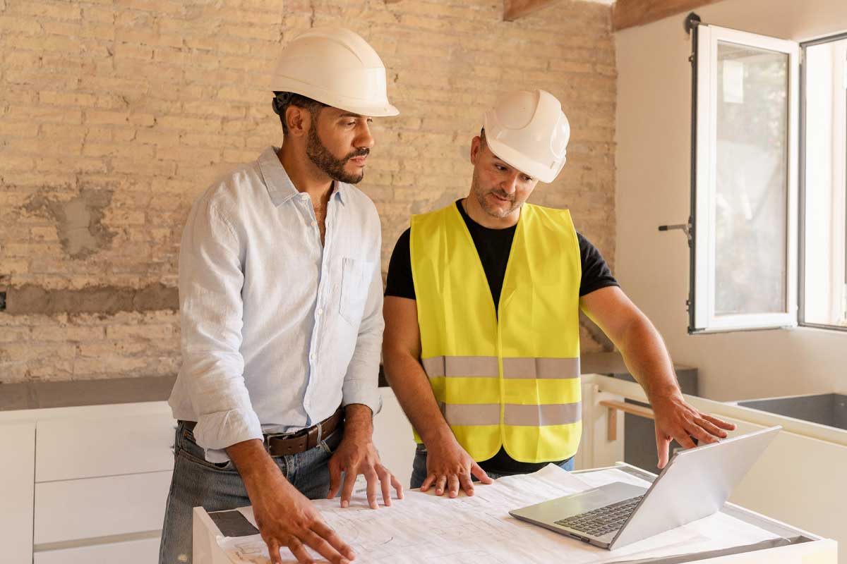 Architect and contractor discussing blueprint using laptop during house renovation